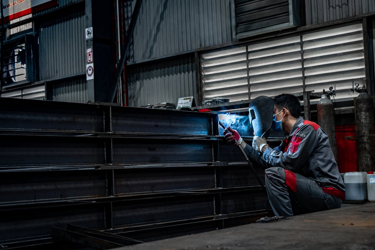 Home Skilled welder working diligently on metal structures inside a warehouse.