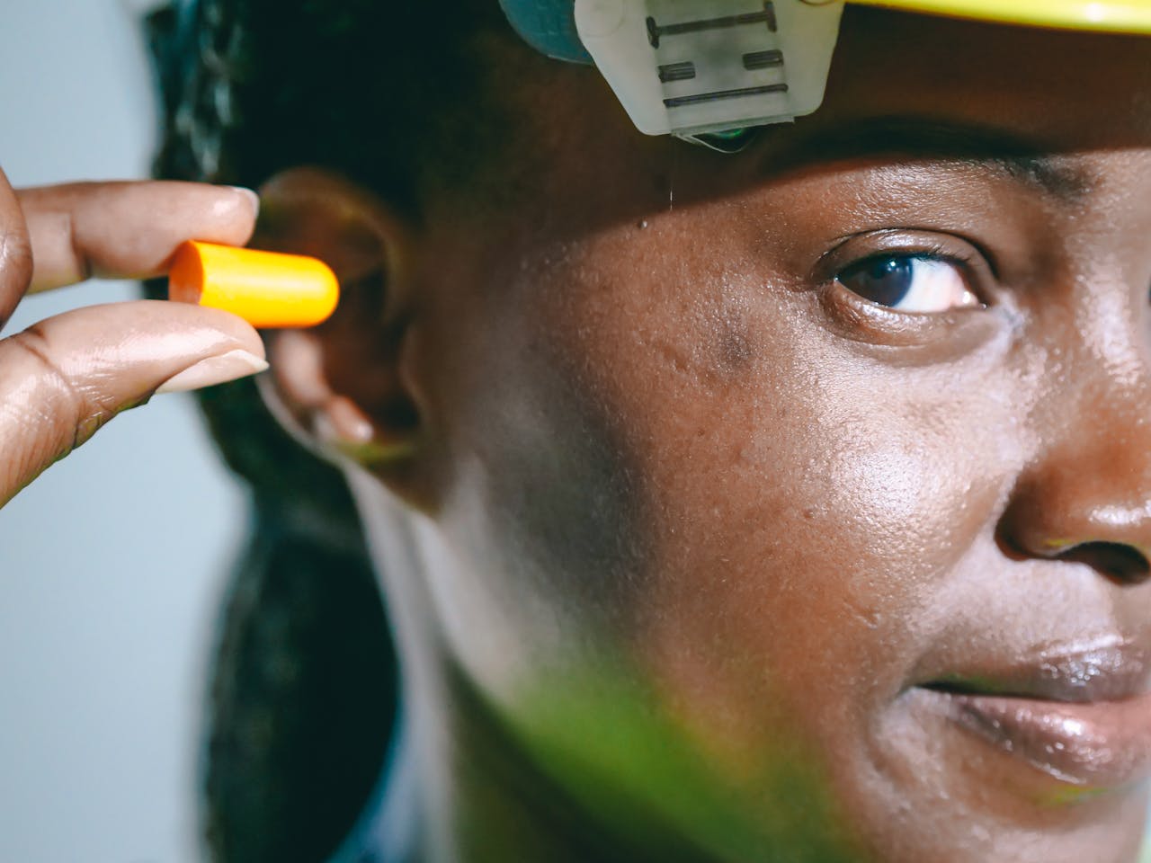 Home A close-up image of a woman inserting an earplug, wearing safety gear.